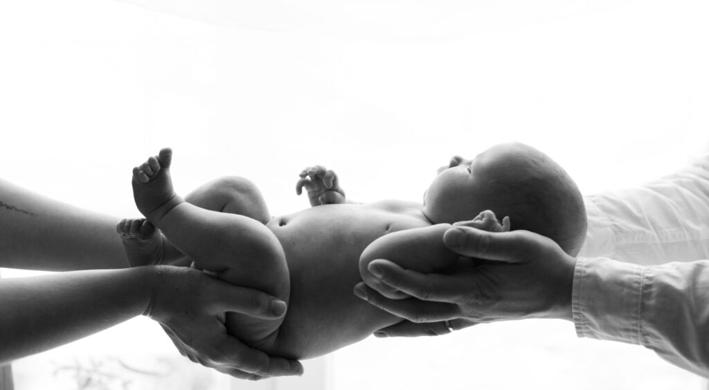 Nyfödd flicka fotograferad inomhus i naturligt ljus, insvept i mjuka filtar, med mamma och pappa i några av bilderna.