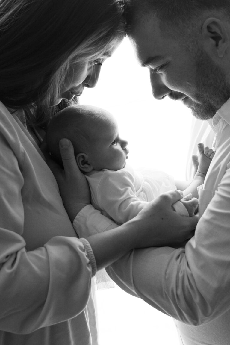 Nyfödd flicka fotograferad inomhus i naturligt ljus, insvept i mjuka filtar, med mamma och pappa i några av bilderna.